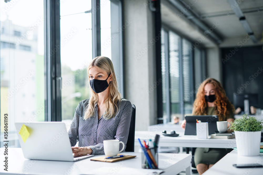 Young people with face masks back at work or school in office after lockdown. - obrazy, fototapety, plakaty 