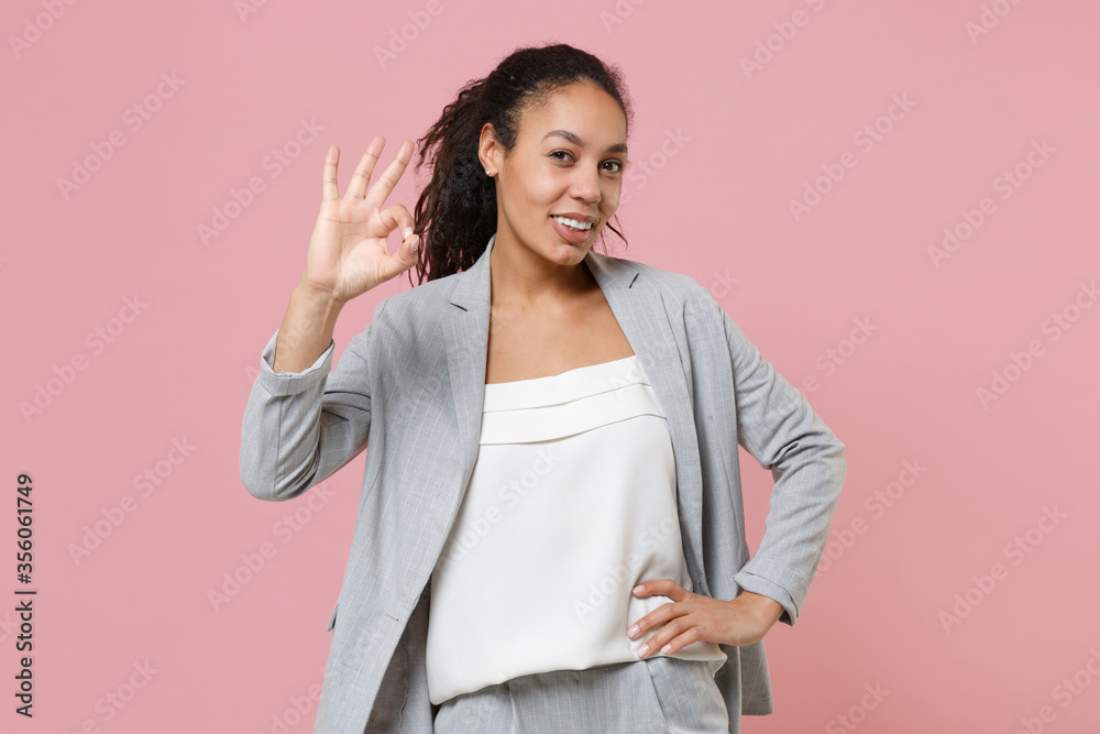 Smiling young african american business woman in grey suit, white shirt isolated on pink background studio portrait. Achievement career wealth business concept. Mock up copy space. Showing OK gesture. Smiling young african american business woman in grey suit, white shirt isolated on pink background studio portrait. Achievement career wealth business concept. Mock up copy space. Showing OK gesture.