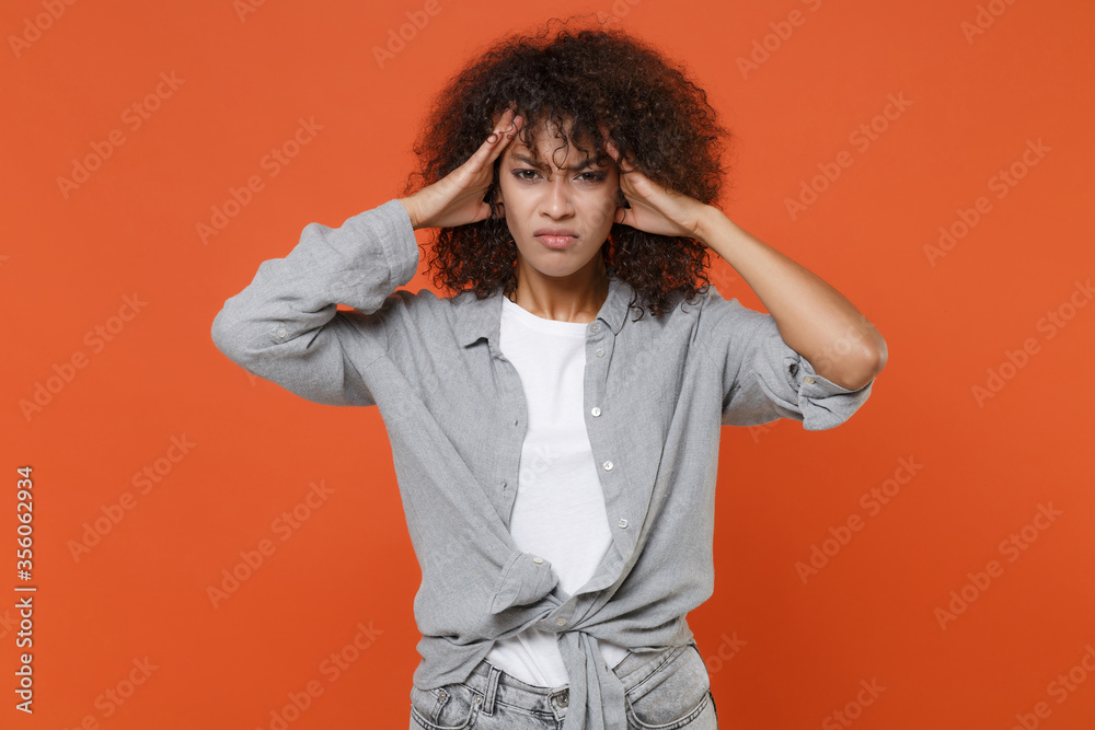 Tired displeased young african american woman girl in gray casual clothes posing isolated on orange background studio. People lifestyle concept. Mock up copy space. Put hands on head, having headache. Tired displeased young african american woman girl in gray casual clothes posing isolated on orange background studio. People lifestyle concept. Mock up copy space. Put hands on head, having headache.