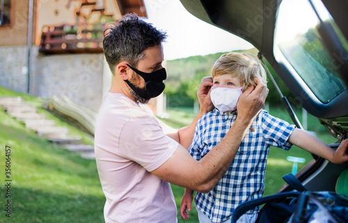Father with small son going on trip by car, wearing face masks.