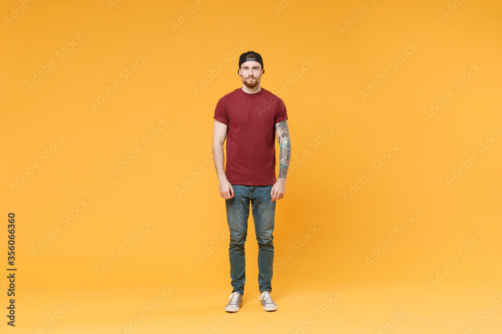 Fototapeta premium Handsome young tattooed man guy in casual t-shirt black cap posing isolated on yellow wall background studio portrait. People sincere emotions lifestyle concept. Mock up copy space. Looking camera.
