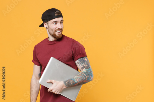 Quadro em tela Amazed young bearded tattooed man guy in casual t-shirt black cap posing isolated on yellow background in studio