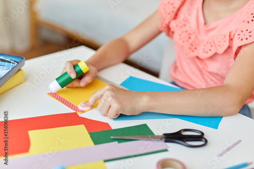 childhood, creativity and hobby concept - close up of creative girl making greeting card and sticking paper stripe with glue stick at home
