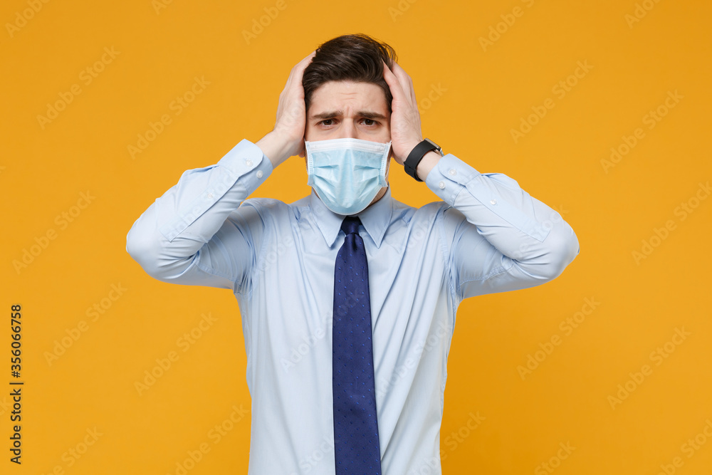 Displeased young business man in classic blue shirt tie sterile face mask isolated on yellow background. Epidemic pandemic coronavirus 2019-ncov sars covid-19 flu virus concept. Put hands on head. Displeased young business man in classic blue shirt tie sterile face mask isolated on yellow background. Epidemic pandemic coronavirus 2019-ncov sars covid-19 flu virus concept. Put hands on head.