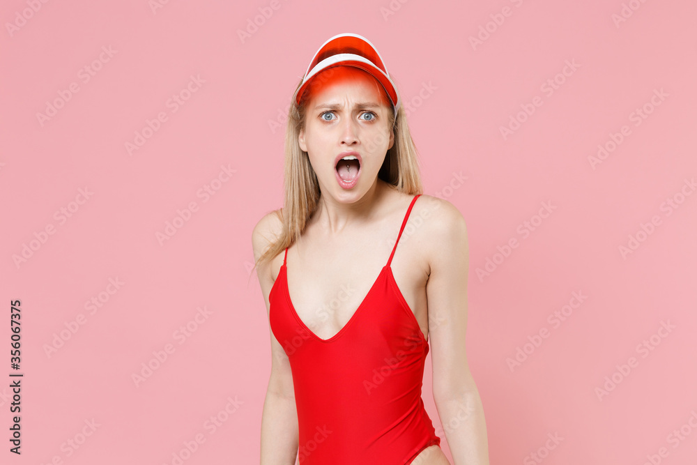 Shocked nervous young blonde woman girl in red one-piece swimsuit cap posing isolated on pink background studio. People summer vacation rest lifestyle concept. Mock up copy space. Keeping mouth open. Shocked nervous young blonde woman girl in red one-piece swimsuit cap posing isolated on pink background studio. People summer vacation rest lifestyle concept. Mock up copy space. Keeping mouth open.