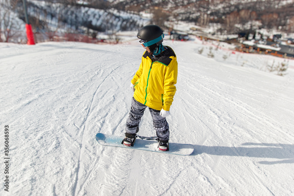 Snowboarder in black helmet, yellow jacket glides down on a blue snowboard on the ski slope