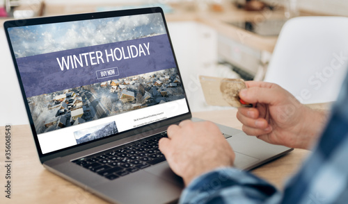 Booking online hotels or winter holidays concept. Man holding credit card and chooses winter holidays on the Internet sitting at home