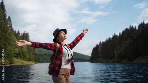 Schilderij op canvas Young woman standing by lake on a walk outdoors in summer nature, relaxing