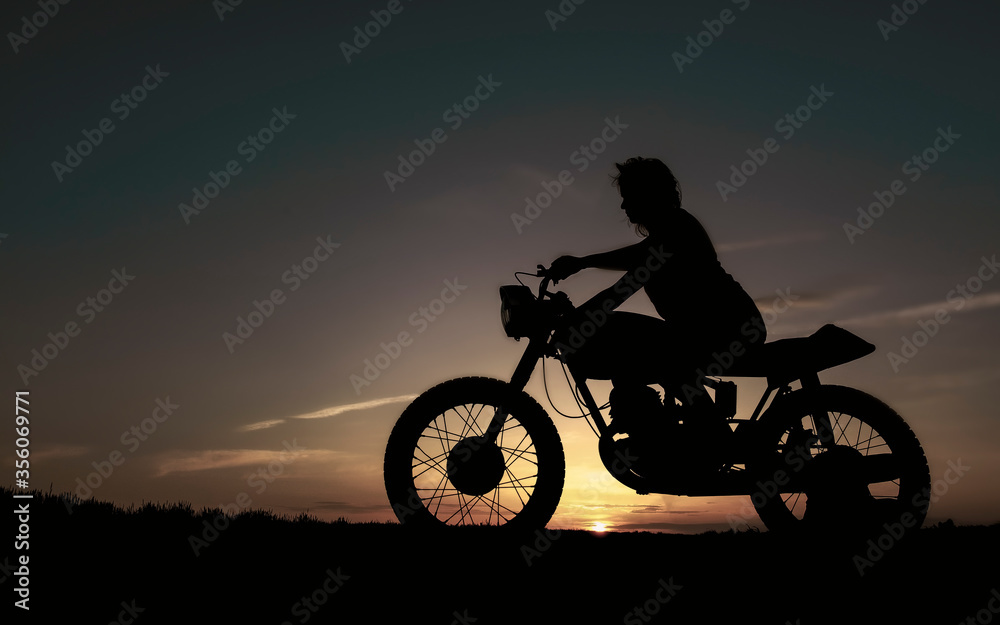 Obraz premium Shadow of a biker girl on a sunset background, silhouette of a girl on a bike. Black motorcycle and a woman on it.