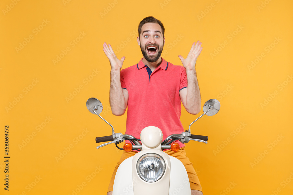 Surprised young bearded man guy in casual summer clothes driving moped isolated on yellow background. Driving motorbike transportation concept. Mock up copy space. Keeping mouth open, spreading hands.