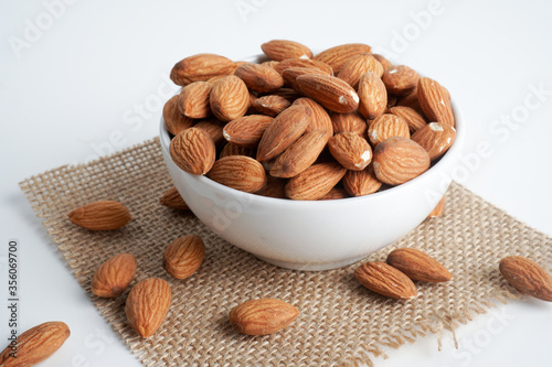 almonds in white bowl and glass of milk and brown fabric on white background. top view and flat lay, 
