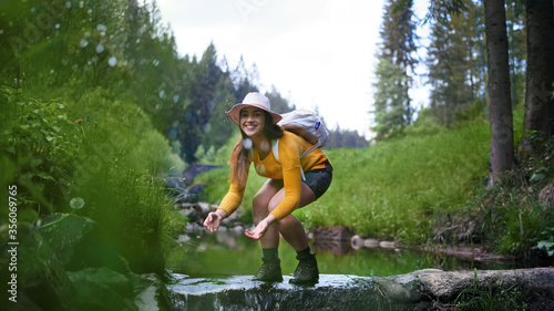Fototapeta Naklejka Na Ścianę i Meble -  Happy young woman standing by stream on a walk outdoors in summer nature.