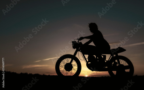 Shadow of a biker girl on a sunset background, silhouette of a girl on a bike. Black motorcycle and a woman on it.
