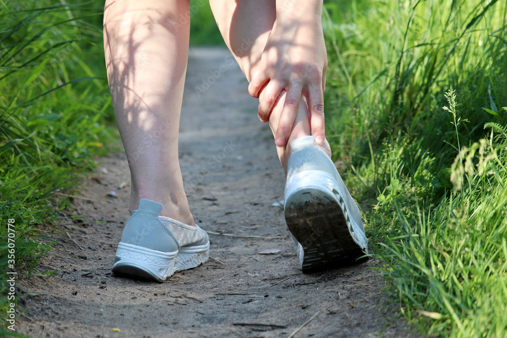 Ankle sprain, woman grabbed her leg while walking on a summer nature. Concept of tired legs, injury on running