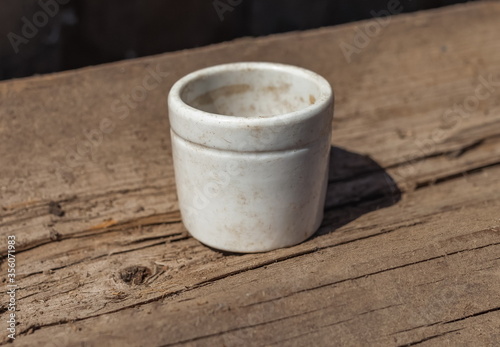 Old white ceramic salt shaker close - up against a wooden log