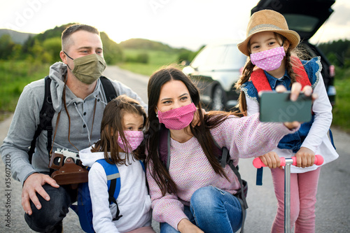 Family with two small daughters and face masks on trip outdoors in nature, taking selfie. © Halfpoint