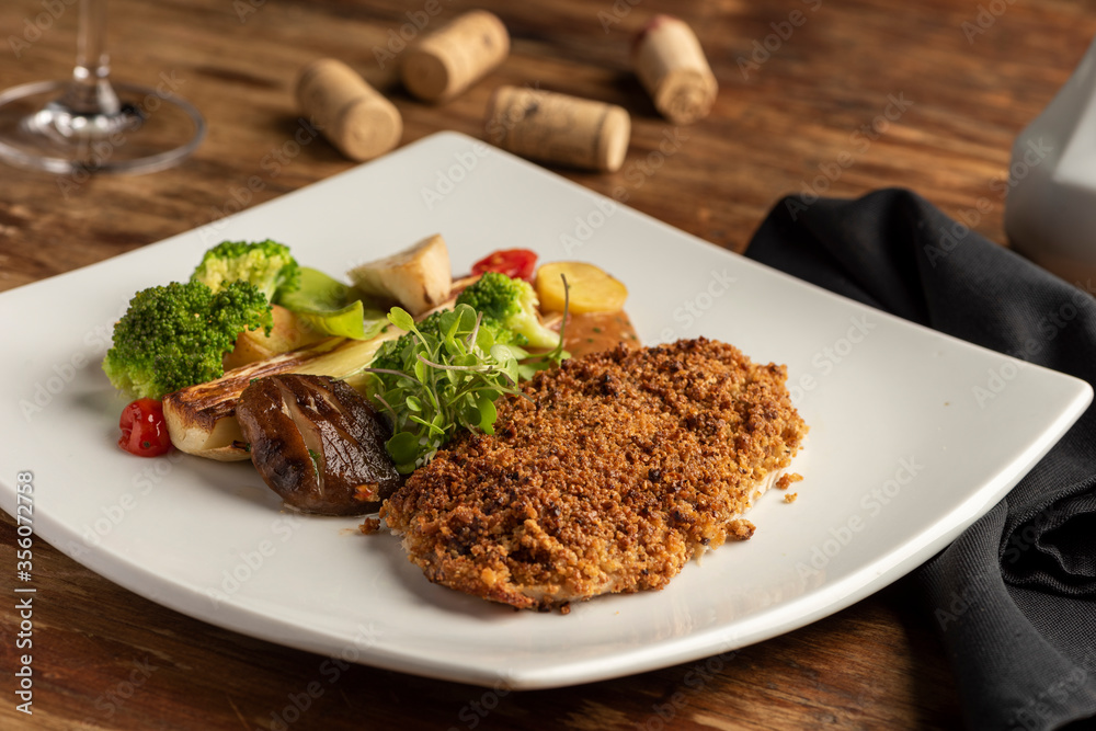 fish baked with crust and vegetables on white plate on a wooden table