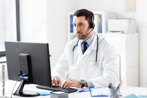 healthcare, medicine and technology concept - male doctor with computer and headset working at hospital