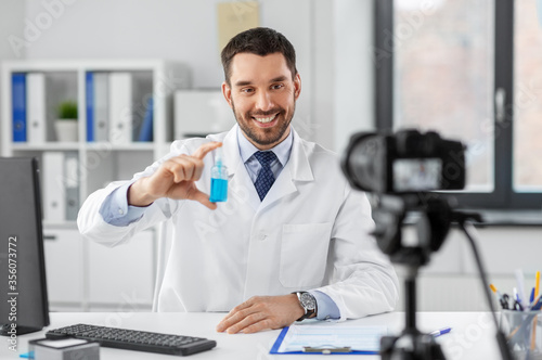 healthcare, medicine and blogging concept - happy smiling male doctor with camera and hand sanitizer recording video blog at hospital