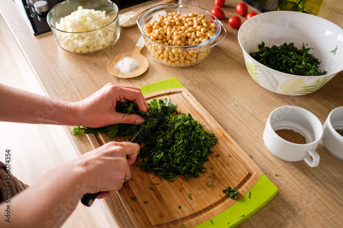 Woman hands, cutting dill while preparing ingredients for falafel. Healthy diet