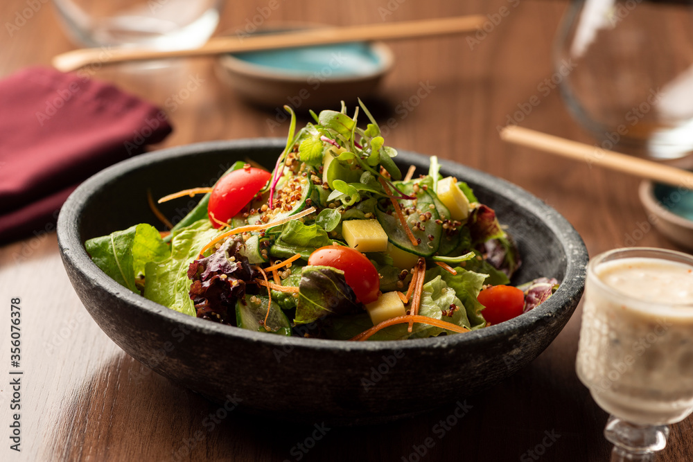 Green salad with lettuce arugula tomatoes on a ceramic bowl and dressing on cup Green salad with lettuce arugula tomatoes on a ceramic bowl and dressing on cup