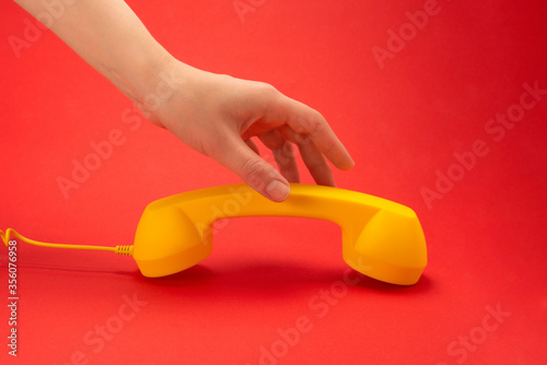 Yellow handset on a red background in woman hand.