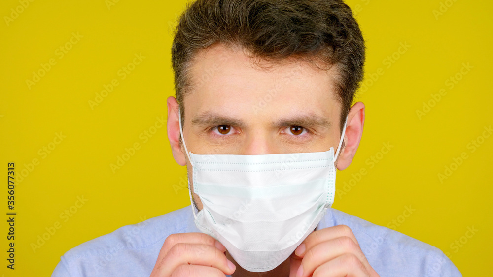 Close up an infectious disease doctor puts on a protective medical mask for examination of patients. Man on a yellow background