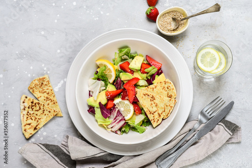 Green vegan salad from green leaves mix and vegetables. Top view on gray stone table. avocado strawberries salad with vegetables and leaves. pieces of fresh tortilla on the plate. © KEA