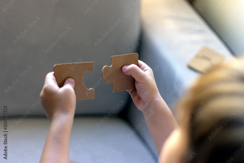 Two blank white puzzle pieces in boys hands.Little boy is trying to connect couple jigsaw puzzle piece.Boys holding in hands two puzzle pieces up in the air,trying to put them together.Copy space.