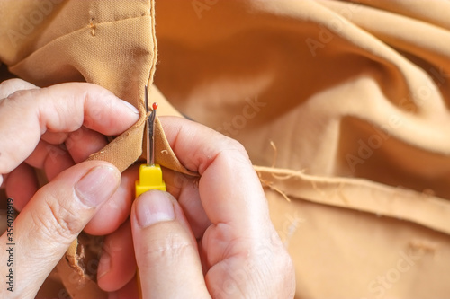 Hands of seamstress is using a seam ripper to rip out thread of the seam of the brown trousers with copy space close-up.