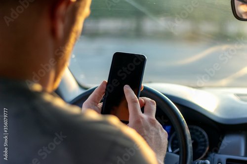 Close up shot of man using smartphone to find direction while driving.Cropped shot of man using mobile in car.Rear view of young male using mobile device for text messages.Driver hands holding phone.