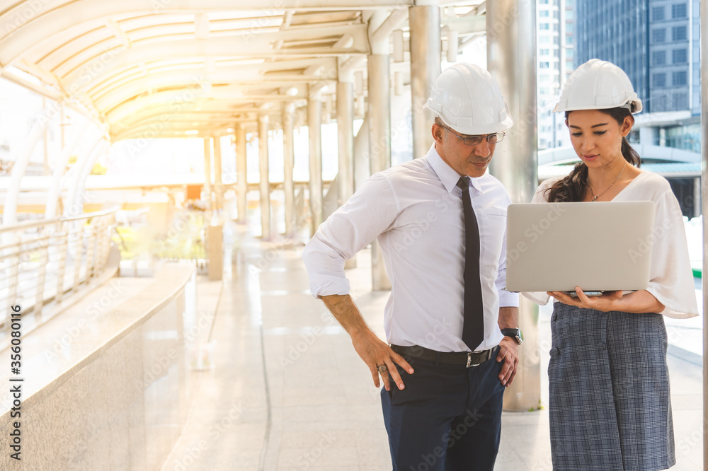 Two engineers man and woman in construction in white helmets working outdoor office building. Two engineers man and woman in construction in white helmets working outdoor office building.