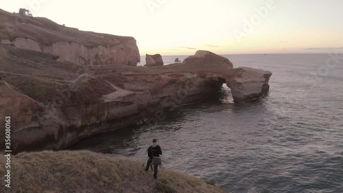 Man taking picture at the coastline at Tunnel beach, Dunedin, New Zealand during sunrise.