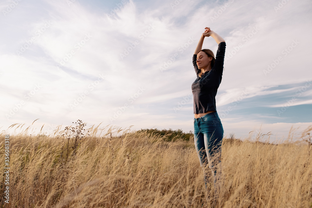 Young woman enjoying nature and freedom in a golden field under the blue sky Young woman enjoying nature and freedom in a golden field under the blue sky