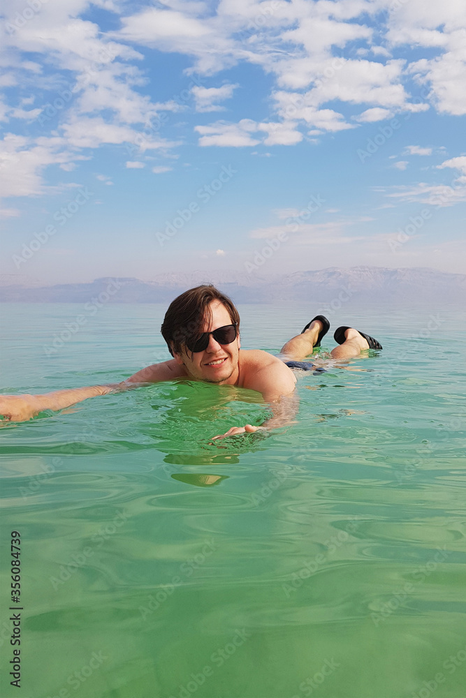 A young man / guy is floating in the waters of the Dead Sea, the coast of Israel. Wellbeing and relaxing concept. Vertical photo.