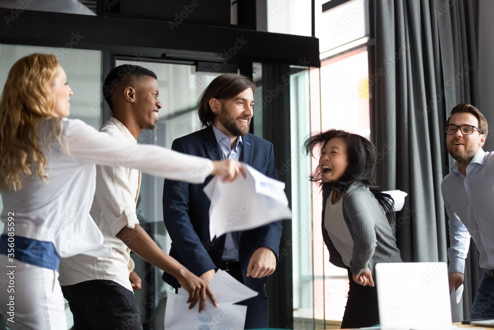 Fototapeta premium Emotional crazy multiracial staff members screaming with joy dancing having fun moving listens music celebrating promotion, award, monetary reward, common business success, salary growth day concept