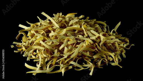 Raw tagliatelle pasta noodles with turmeric isolated on black background
