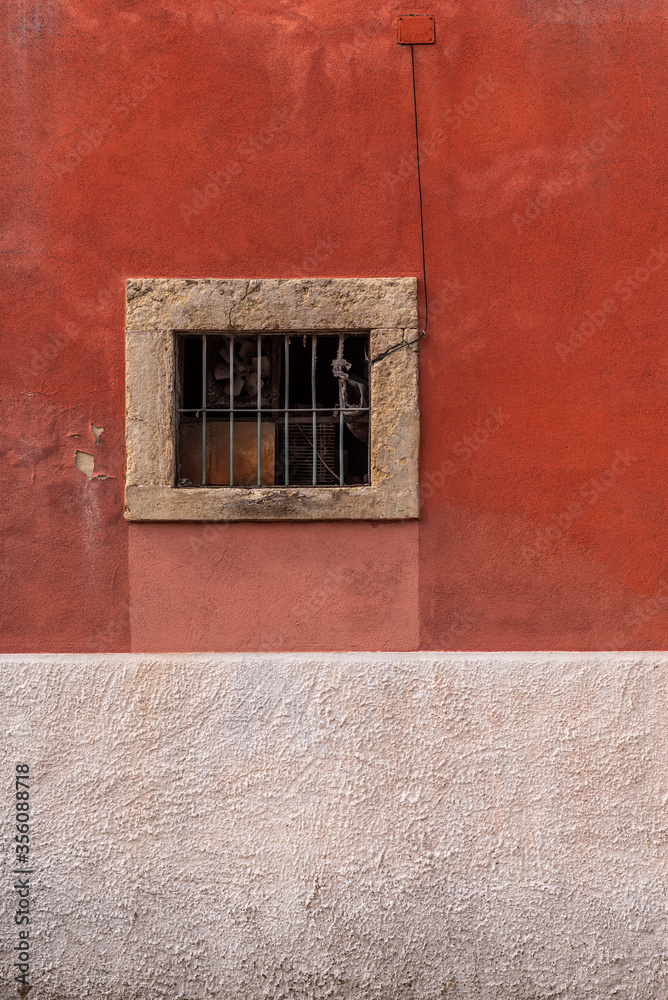 Antique building painted washed red facade and a window with metallic bars framed on stone
