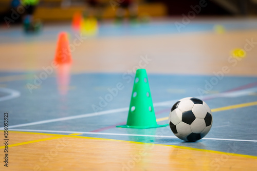 Futsal practice pitch. Indoor soccer ball and training equipment on the wooden floor. Football training cones and markers in the blurred background