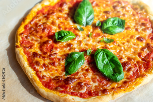 Close-up detail shallow focus view of baked tasty hot homemade italian Margarita pizza on baking paper just picked from oven. Melted mozzarella cheese , tomato sausw and fresh green basil topping