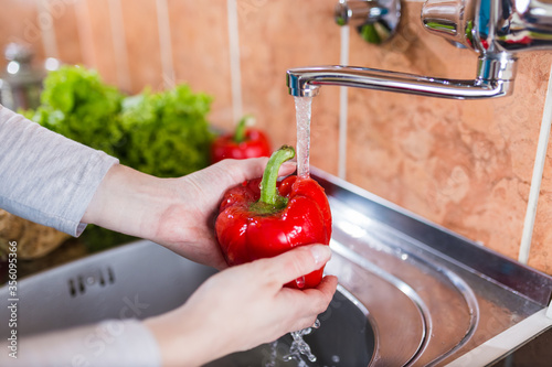 Close up of woman hands washing bell pepper in modern kitchen.