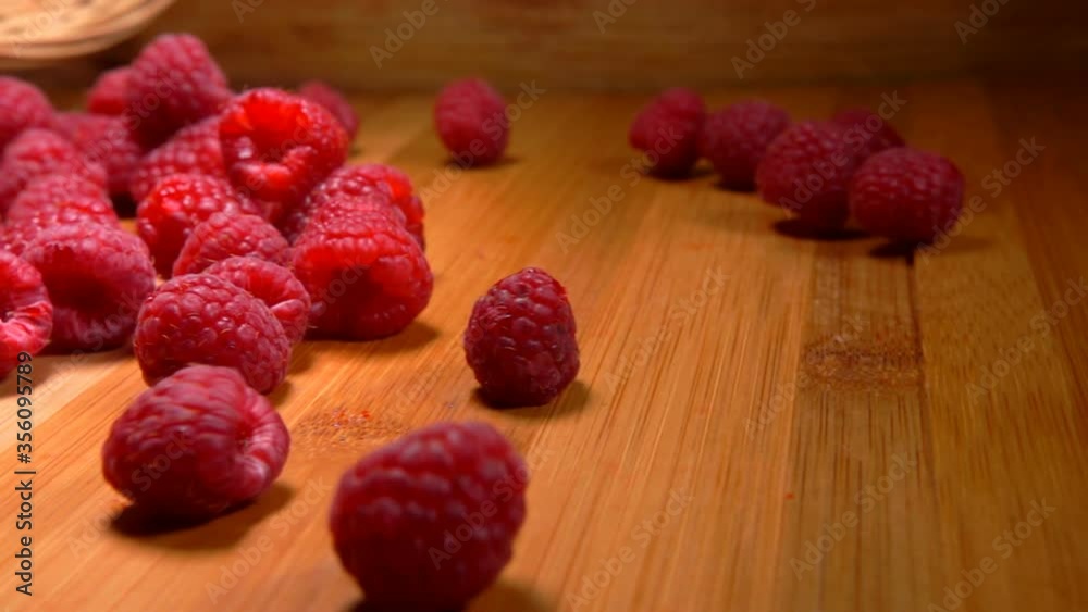 Close up of a large juicy appetizing raspberries falling from the wicker basket to the wooden table Close up of a large juicy appetizing raspberries falling from the wicker basket to the wooden table