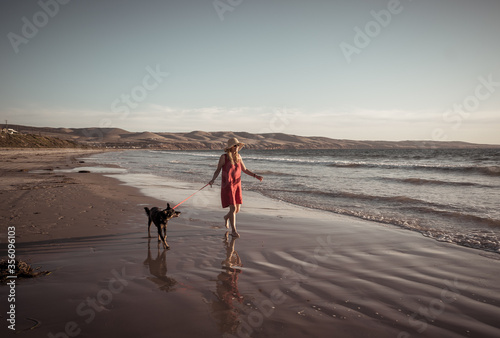 Mature woman and pet dog walking together on empty beach in the new normal after coronavirus