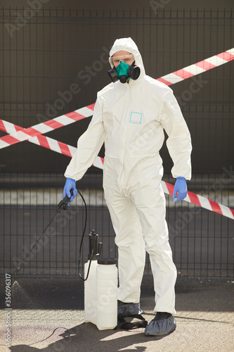 Wallpaper Mural Vertical full length portrait of male worker wearing hazmat suit holding disinfection gear while standing outdoors with red caution tape in background Torontodigital.ca