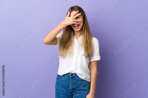 Young woman over isolated purple background covering eyes by hands and smiling © luismolinero