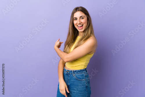 Young woman over isolated purple background pointing back