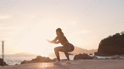 sporty woman squats workout on beach. Beautiful fitness model butt workout outdoors. Sunset beach with sea view background.