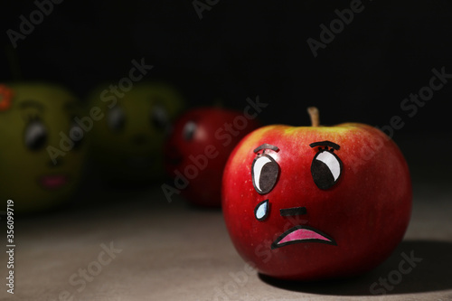 Apple with crying face on grey table, closeup. Concept of jealousy