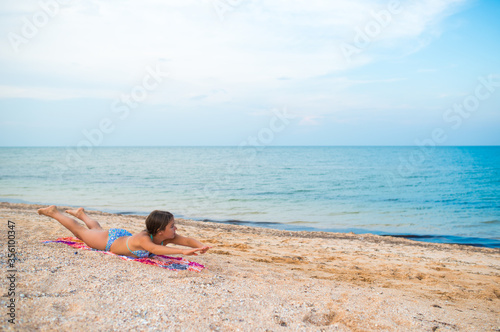 Charming little girls do gymnastic exercises while relaxing on the beach on a sunny warm summer day. The concept of sports and active games in the summer. Copyspace