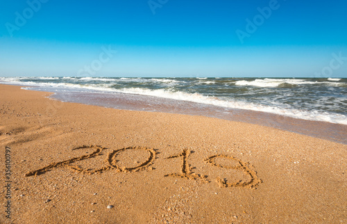 Inscription on sand 2019 the backdrop of a noisy blue sea and blue sky on a sunny warm summer day during vacation. Concept Travel and Tourism Planning in the 19 Year